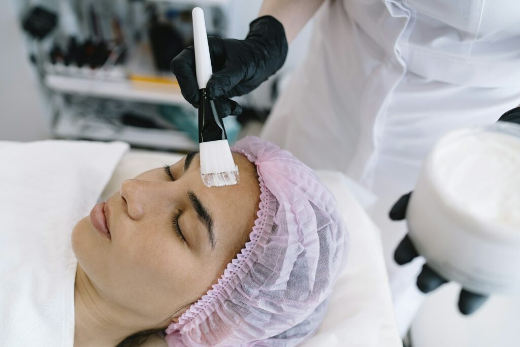 Crop cosmetologist applying cosmetic mask in beauty salon