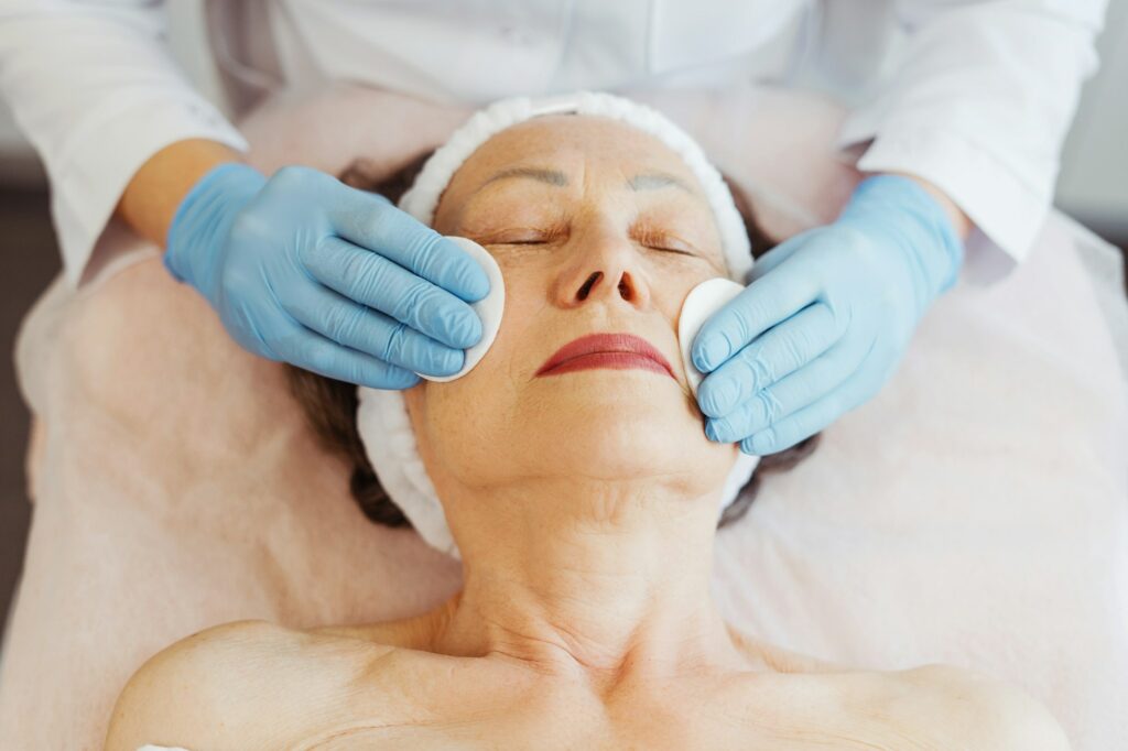 Senior, elderly woman lying in cosmetic clinic doctor in latex gloves performing cosmetic procedures